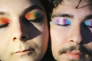 portrait of closeup faces of two lgbtq queer friends faces with rainbow pride flag and trans pride flag makeup / eyes closed - obrazy, fototapety, plakaty