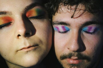 portrait of closeup faces of two lgbtq queer friends faces with rainbow pride flag and trans pride flag makeup / further version