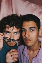portrait of two queer young men with trans pride flag eye makeup and pink background / on gender...