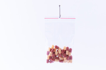 The Pharmaceutical Trap and Drug Addiction - Colored Pills or Tablets Hanging in Small Ziplock Bag on a Fishing Hook Against the White Background