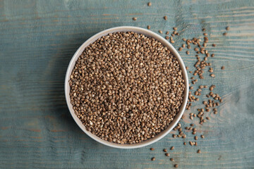 Bowl with organic hemp seeds on light blue wooden table, flat lay