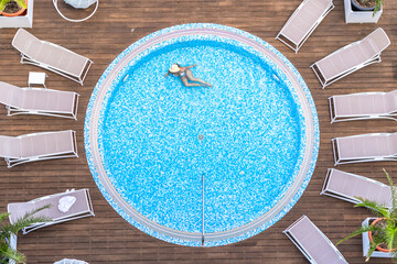 Young alone beautiful sports woman in bikini and hat is swimming in hydro massage bath on wooden...