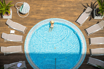 Young alone beautiful sports woman in bikini and hat is swimming in hydro massage bath on wooden...