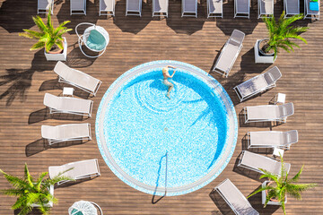Young alone beautiful sports woman in bikini and hat is swimming in hydro massage bath on wooden...