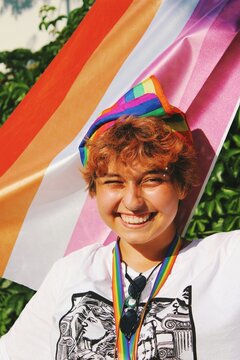 portrait of queer young woman smiling & holding lesbian pride flag in city street pride parade

