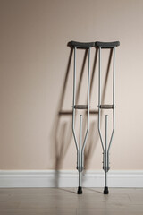 Pair of axillary crutches near beige wall. Space for text