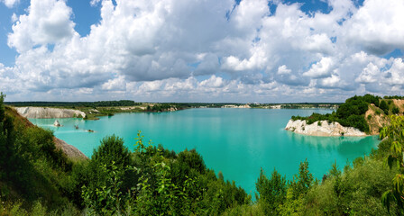 An old chalk quarry overgrown with green young plants with clear  turquoise water. Technogenic mountains formed during chalk mining. Panoramic view