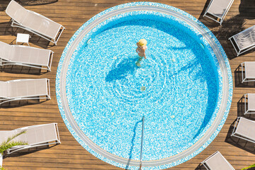 Young alone beautiful sports woman in bikini and hat is swimming in hydro massage bath on wooden terrace. Aerial drone view. Tropical summer luxury hotel