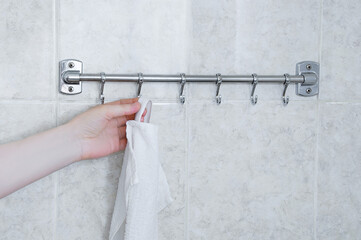 Hangs a white towel on a metal hanger in bathroom.
