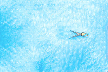Obraz premium Top view of young woman in bikini and straw hat is swimming in transparent blue sea, lagoon. Aerial, drone view