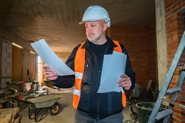 Foreman builder of builders examines a sheet of paper. Builder inside an unfinished building....