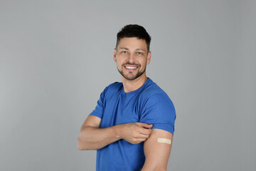 Vaccinated man with medical plaster on his arm against grey background