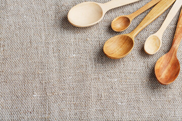 Craft spoons made from different types of wood lie in a row on a hemp burlap fabric. Top view, free space