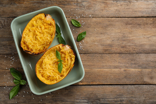 Halves of cooked spaghetti squash in baking dish, basil and salt on wooden table, flat lay. Space for text