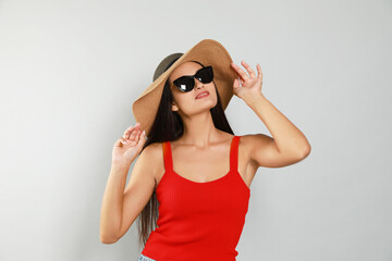 Beautiful young woman with straw hat and stylish sunglasses on light grey background