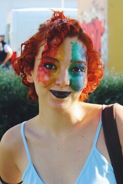 portrait of queer young woman smiling with lgbtqia rainbow pride flag facepaint in pride parade , city background