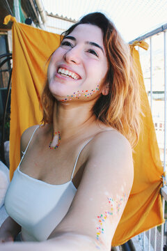Happy smiling portrait of young woman with vitiligo on skin & colorful paint around spots and yellow background / body image, self love and celebration