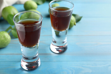 Delicious liqueur and green walnuts on light blue wooden table, closeup. Space for text