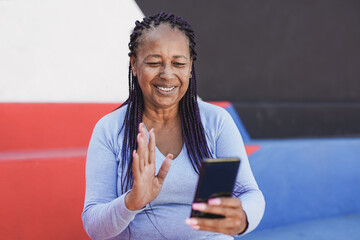 Senior african woman with braided hairs using smartphone for doing video call while waving hand