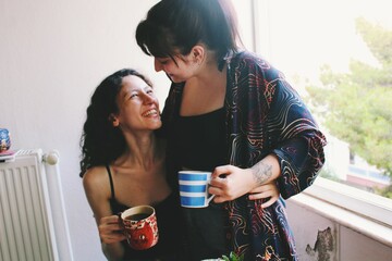happy portrait of two women / lesbian couple at home cuddling smiling & drinking coffee *2