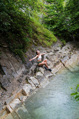 Young happy woman enjoing the nature, sitting by the mountain river.