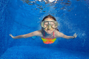 Happy young girl in snorkeling mask dive underwater in the pool.