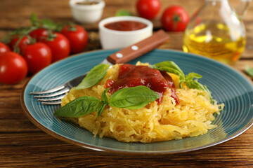 Tasty spaghetti squash with tomato sauce and basil served on wooden table, closeup