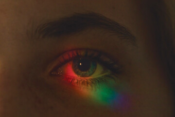 Close up of a blue eye in darkness illuminated with rainbow