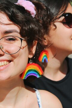 two women friends smiling with glasses wearing rainbow pride flag themed earrings