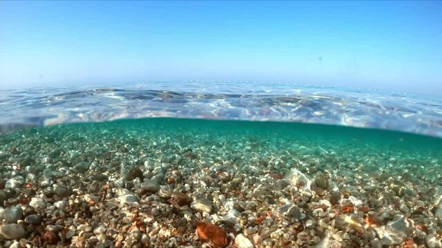 Slow-motion half underwater video at the border of air and water. Beautiful rocky beach on the Adriatic Sea in Montenegro.