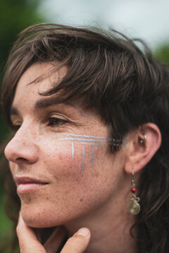 Beautiful woman with brown hair, freckles, silver tribal facepaint