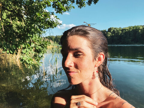 natural woman in green forrest lake smiles with dragonfly on head