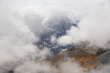 Clouds fly over the mountain valley. Mountain peaks between clouds. Photo from above. Soft focus. Selective focus on hills.