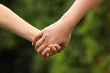 Woman and child holding hands outdoors, closeup