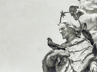 Fototapeta na wymiar Pigeon sitting on a unknown statue of a saint in Liberty Square, Timisoara