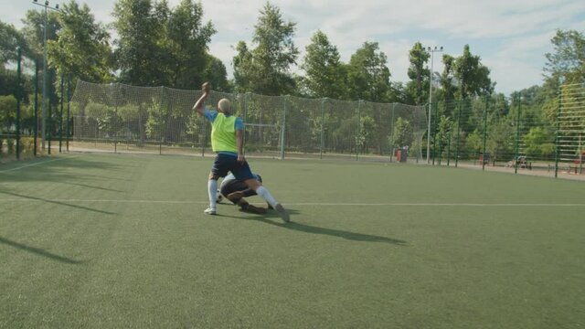 Soccer defender committing foul against opponent offensive player during game on football pitch at daybreak. Soccer striker falling down on sports field after push harsh by defender during match