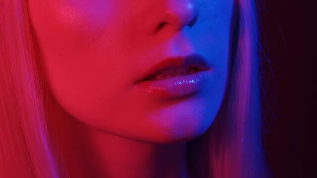 Shiny juicy female lips in neon light. The woman breathes half-heartedly and opens her mouth. Multi-colored lights illuminate her face. Night deep, parties. Close-up, 4K UHD.