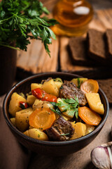 Tasty cooked dish with potatoes in earthenware on wooden table, closeup