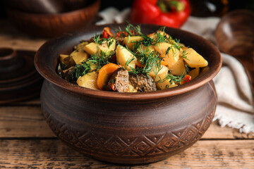 Tasty cooked dish with potatoes in earthenware on wooden table