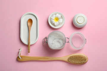 Body scrub, plumeria flower and brush on pink background, flat lay