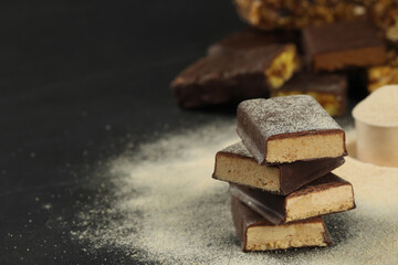 Tasty energy bars and protein powder on black table, space for text