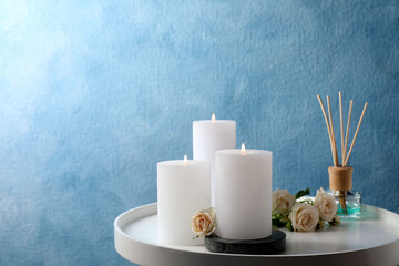 Burning candles, air reed diffuser and beautiful roses on white table near light blue wall, space...