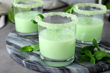 Delicious mint liqueur with ice cubes and green leaves on grey table, closeup