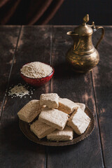 Pieces of tahini halva, sesame seeds in a bowl, an vintage jug.