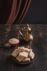 Pieces of tahini halva, sesame seeds in a bowl, an vintage jug.