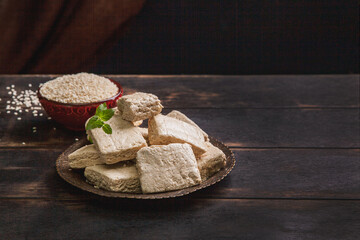 Pieces of tahini halva, sesame seeds in a bowl, an old brown wooden background, copy space
