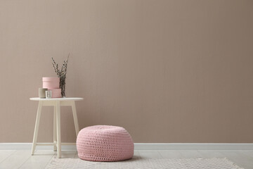 Knitted pouf and decor elements near beige wall indoors. Space for text