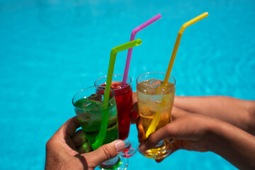 Three multi-colored cocktails red, yellow and green in the hands of friends on a background of blue sea water. Summer vacation concept. 