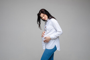 Beautiful female expecting baby, touch pregnant belly feeling pain on gray studio background....