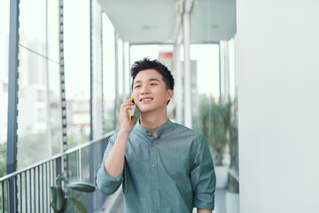 Happy man speaking on cellphone standing on balcony in city in summer day